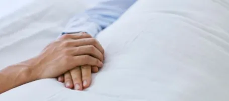 Person holding hands in hospital beds